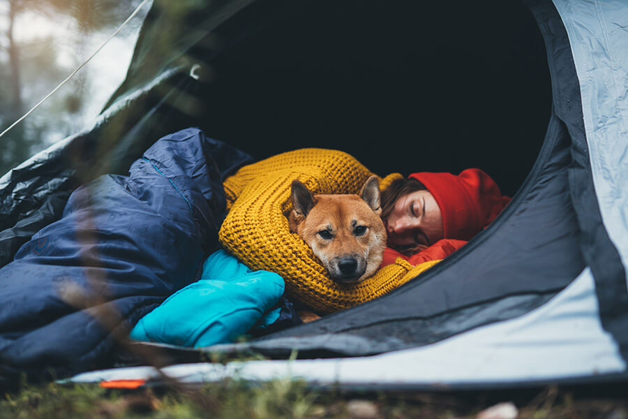 Frau mit Hund eingekuschelt in Schlafsack